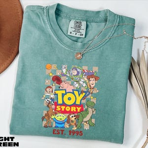 A green t-shirt with a graphic of characters from the Toy Story movie, including Woody, Buzz Lightyear, and other beloved characters, along with the text "TOY STORY EST. 1995".