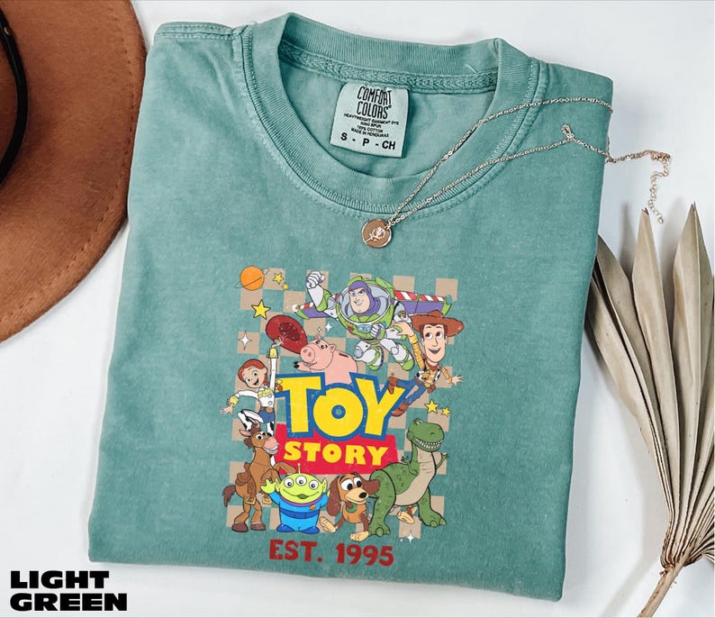 A green t-shirt with a graphic of characters from the Toy Story movie, including Woody, Buzz Lightyear, and other beloved characters, along with the text "TOY STORY EST. 1995".