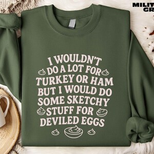 A green sweatshirt with white text printed on it, placed on a surface with a mug and some white flowers.