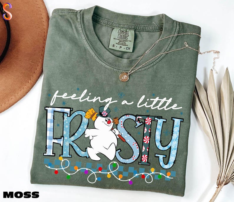 A green t-shirt with a snowman graphic and the text "feeling a little FROSTY" printed on it, along with a necklace and a hat.