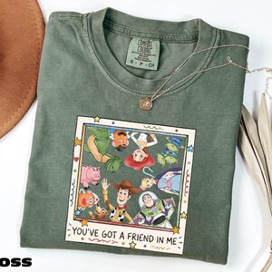 A green t-shirt with a graphic of characters from the Toy Story movie, including Woody, Buzz Lightyear, and other beloved characters, along with the text "You've Got a Friend in Me".