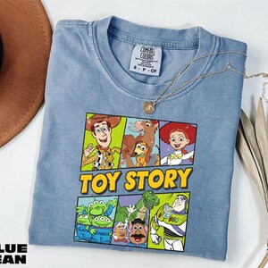 A blue t-shirt with a cartoon character design, including characters from the Toy Story franchise, is displayed on a white surface.