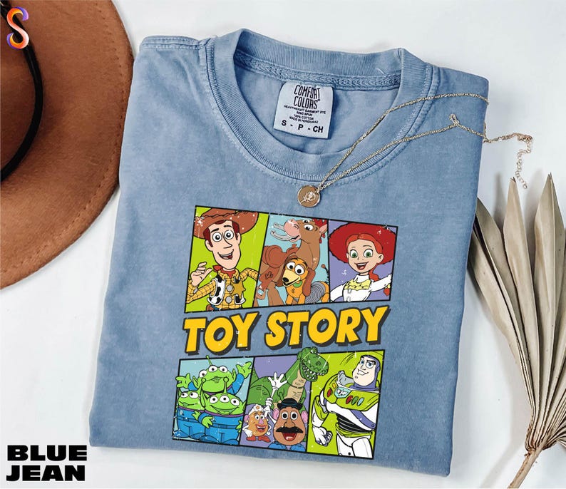 A blue t-shirt with a cartoon character design, including characters from the Toy Story franchise, is displayed on a white surface.