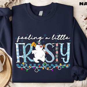 A navy blue sweatshirt with a snowman graphic and the text "feeling a little FRISKY" printed on it.