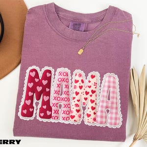 a purple t-shirt with the word "MAMA" printed on it, along with a necklace and a hat.