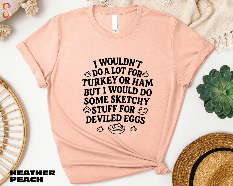a pink t-shirt with a humorous text printed on it, along with some other items such as a hat, a plant, and a bowl.