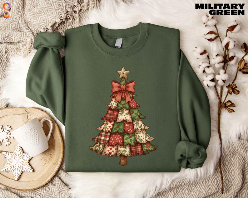 A green sweater with a Christmas tree design printed on it, placed on a white fur rug. There is also a mug and some white flowers in the background.