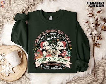 May include: Forest green sweatshirt featuring Mickey and Minnie Mouse enjoying hot cocoa. The design includes the text "Mickey & Minnie's Hot Cocoa" and "Warm & Delicious, Old Fashioned, Freshly Made Since 1928". The sweatshirt has long sleeves.