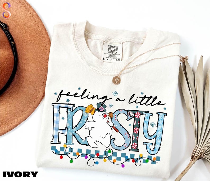 A white t-shirt with a snowman graphic and the text "feeling a little FROSTY" printed on it, along with a necklace and a hat.