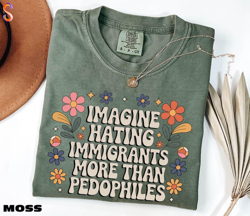 A green t-shirt with a printed message that reads "IMAGINE HATING IMMIGRANTS MORE THAN PEDOPHILES" surrounded by colorful flowers and leaves.