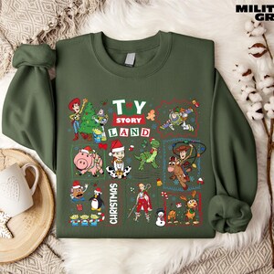 A green sweatshirt with a collage of various characters from the Toy Story franchise, including Woody, Buzz Lightyear, and other beloved characters, along with Christmas-themed elements.