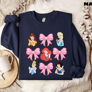 a sweater with princesses on it next to a cup of coffee