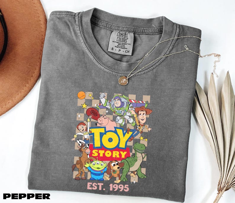 A gray t-shirt with a colorful graphic of characters from the Toy Story movie, including Woody, Buzz Lightyear, and other beloved characters, along with the text "Toy Story" and "Est. 1995".