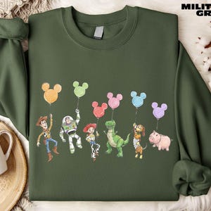 A green sweatshirt with a graphic design featuring characters from the Toy Story movie, including Woody, Buzz Lightyear, Timmy, and other beloved characters.