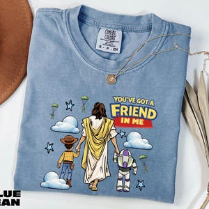 A blue t-shirt with a graphic design depicting a person holding a child and a character from the Toy Story franchise, along with the text "You've got a FRIEND in me".