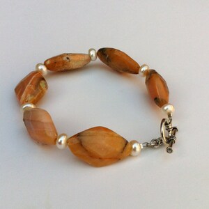 May include: A bracelet with alternating orange agate and white pearl beads. The bracelet has a silver clasp.