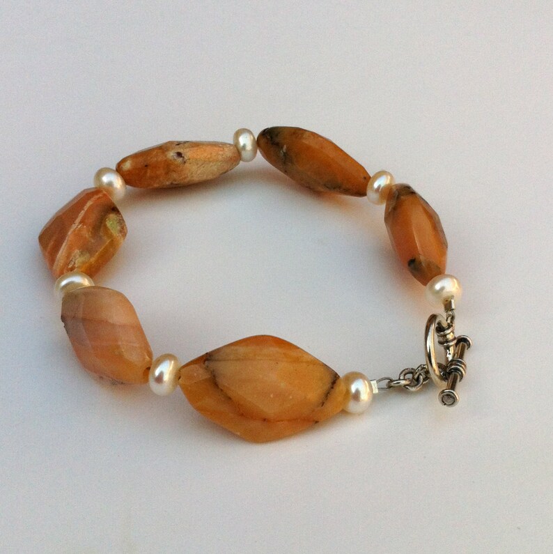 May include: A bracelet with alternating orange agate and white pearl beads. The bracelet has a silver clasp.