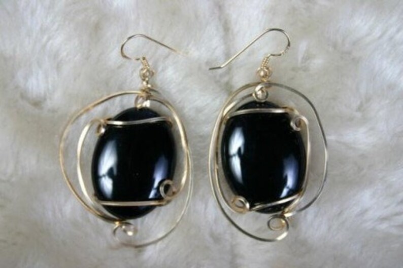 May include: A pair of gold earrings with black oval gemstones set in a wire cage design.