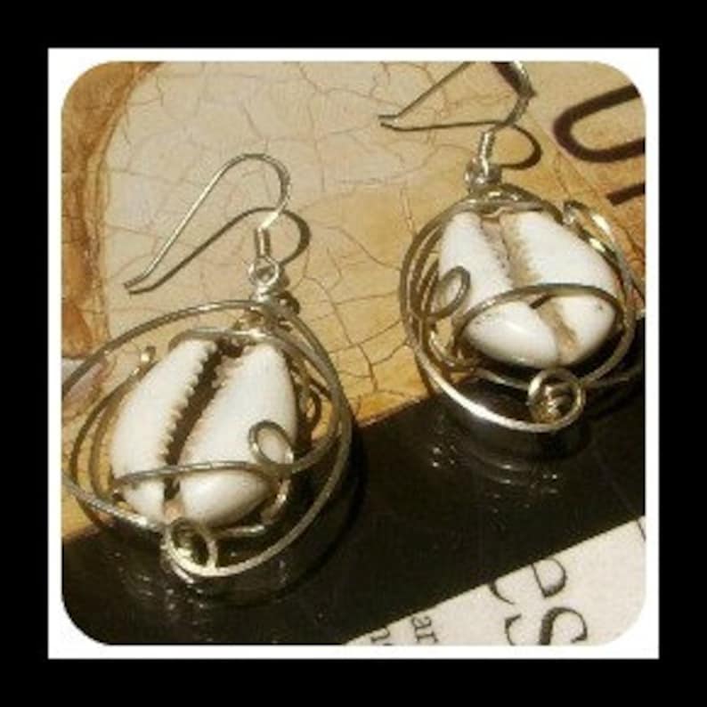 May include: A pair of gold-toned earrings featuring a white cowrie shell encased in a delicate wire design.