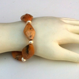 May include: A bracelet made with orange and brown gemstone beads and silver spacer beads.