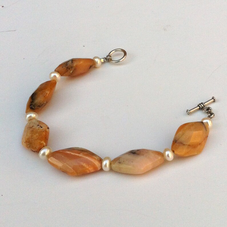 May include: A bracelet made of orange and white beads. The bracelet has a silver clasp and toggle.