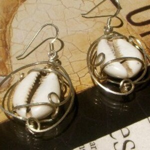 May include: A pair of silver earrings with a white cowrie shell encased in a gold wire cage.