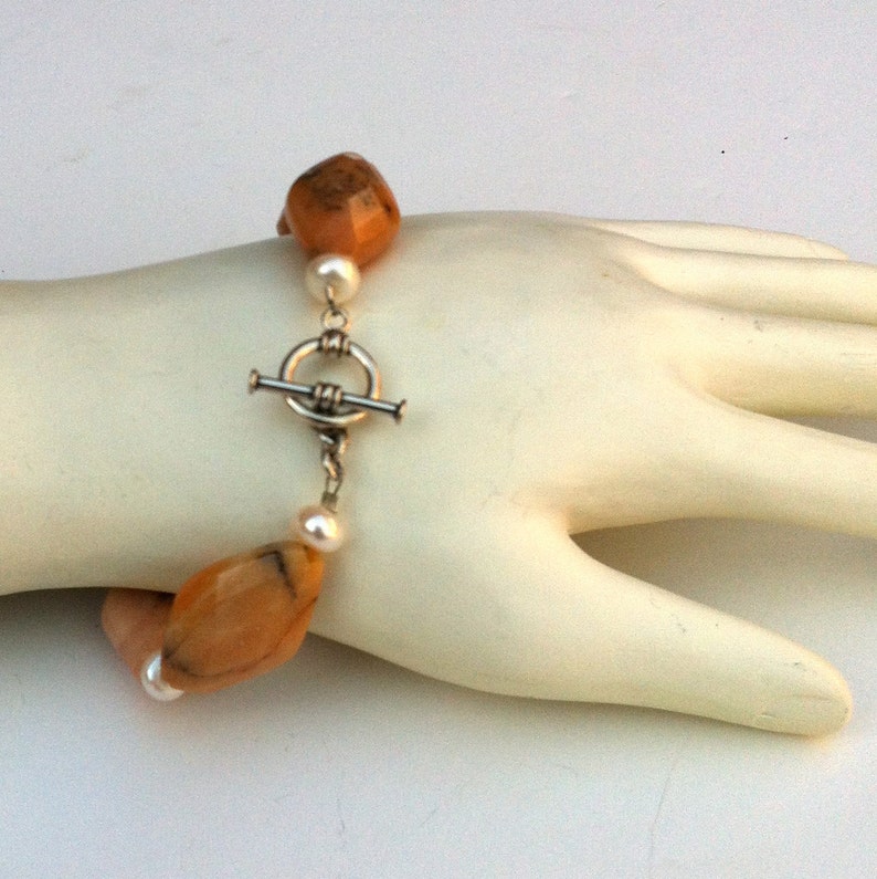 May include: A bracelet with orange and white beads and a silver toggle clasp.
