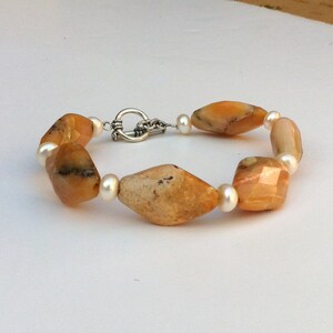 May include: A bracelet made with alternating yellow and white beads. The yellow beads are faceted and have a marbled pattern. The white beads are smooth and round. The bracelet has a silver clasp.