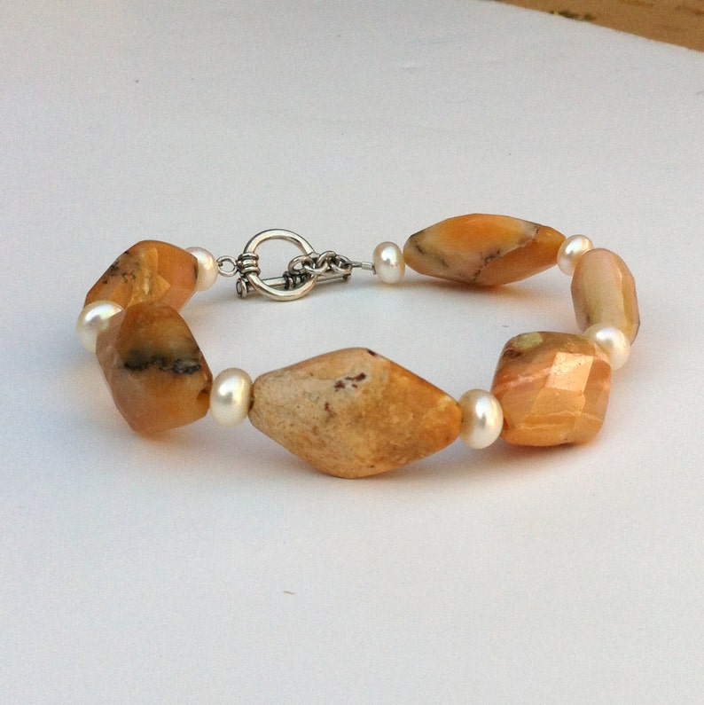 May include: A bracelet made with alternating yellow and white beads. The yellow beads are faceted and have a marbled pattern. The white beads are smooth and round. The bracelet has a silver clasp.