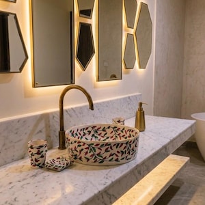 Peut inclure: Une vasque ronde en céramique ornée d'un motif peint à la main de feuilles rouges et vertes sur fond blanc, accompagnée d'un gobelet et d'un porte-savon assortis, posée sur un comptoir en marbre blanc avec un robinet et un distributeur en laiton.