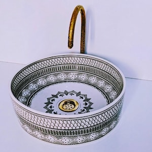 Puede incluir: Un lavabo redondo de cerámica blanca con un patrón geométrico en blanco y negro en el borde y en el centro. Un grifo dorado curvado se arquea sobre el lavabo, añadiendo un toque de elegancia a este accesorio de baño.