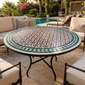 Peut inclure: Une table de salle à manger ronde d'extérieur avec un plateau en mosaïque présentant un motif géométrique dans des tons rouge foncé, vert foncé et blanc. La table repose sur un cadre en métal noir avec quatre pieds incurvés.