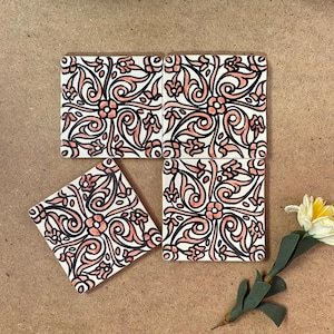 May include: Four square ceramic tiles with a floral design in black, white, and coral. The tiles are arranged in a square pattern, with one tile slightly offset. A single flower with yellow and white petals is in the lower right corner.