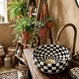 May include: A black and white checkered ceramic sink sits on a wooden surface, paired with a brass faucet. Hanging from a wooden ladder are potted plants in macrame hangers. The scene is a bathroom with a rustic, bohemian aesthetic.