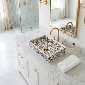 May include: Rectangular bathroom sink with a floral pattern in red, green, and blue on a white background. The sink is set on a white vanity with gold hardware. A gold faucet and mirror are visible.