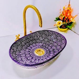 Peut inclure: Lavabo ovale en céramique avec un motif floral violet et blanc. Le lavabo a un drain doré et est associé à un robinet doré. Le lavabo est un élément décoratif de salle de bain.
