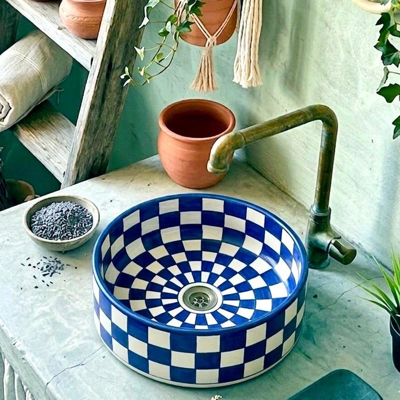 May include: A blue and white checkered ceramic sink with a brass faucet. The sink has a circular design with a drain in the center. A small bowl of lavender sits nearby, along with a terracotta pot and a wooden ladder.