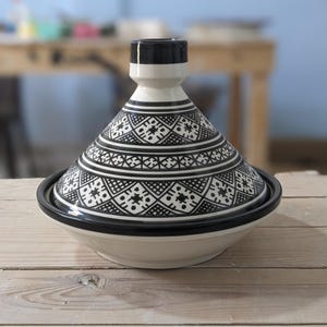 Peut inclure: Une tasse en céramique blanche avec une anse noire et le texte "But First, Coffee" en noir, en gras. La tasse est posée sur une surface blanche.