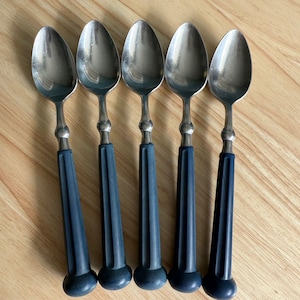 Puede incluir: Conjunto de cinco cucharas de plata con mangos de plástico azul. Las cucharas tienen un cuenco redondeado y un diseño sencillo.