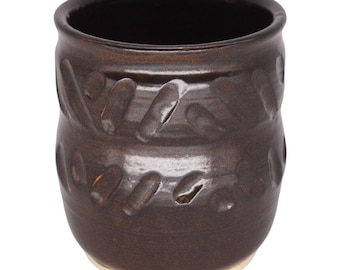 May include: A handmade brown ceramic mug with a dark interior and a light-colored base. The mug features a series of diagonal, oval-shaped indentations around its exterior. The mug is approximately 4 inches tall and 3.5 inches in diameter.