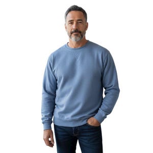 Puede incluir: Una sudadera azul claro con cuello redondo y mangas largas. La sudadera tiene un diseño clásico y está hecha de un material suave. La persona de la imagen lleva vaqueros azul oscuro.