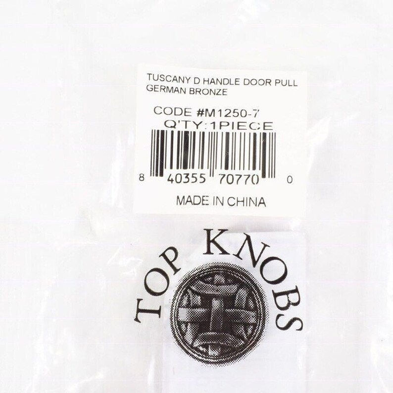 Pode incluir: Uma embalagem contendo uma puxador de porta Tuscany D em bronze alem&atilde;o. O r&oacute;tulo inclui o c&oacute;digo #M1250-7 e a quantidade de 1 pe&ccedil;a. O logotipo Top Knobs tamb&eacute;m &eacute; vis&iacute;vel.