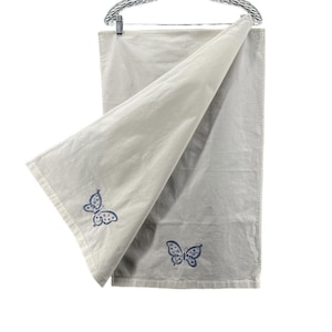 May include: A light gray towel with two embroidered blue butterflies. The towel is hanging from a silver metal bar. The butterflies have a detailed wing pattern.