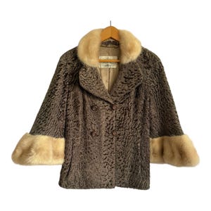 May include: A vintage brown faux fur coat with a light tan collar and cuffs. The coat features a double-breasted design with brown buttons and is hanging on a wooden hanger. The coat's texture appears to be curly.