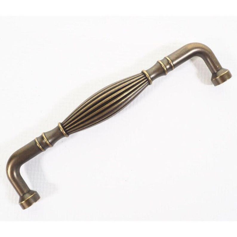 Pode incluir: Puxador de arm&aacute;rio em bronze antigo com centro canelado e extremidades curvas. O hardware foi projetado para f&aacute;cil instala&ccedil;&atilde;o e adiciona um toque vintage aos m&oacute;veis. O puxador mede aproximadamente 15 cm de comprimento.
