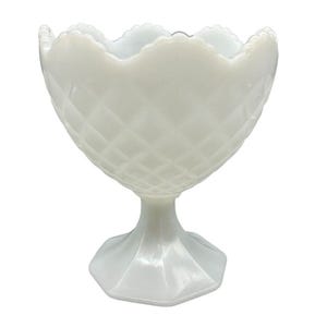 Puede incluir: Un cuenco blanco con pedestal de estilo vintage. El cuenco tiene un patrón de diamantes en el exterior y un borde festoneado. La base tiene forma hexagonal. Esta pieza decorativa es probablemente de vidrio o cerámica.