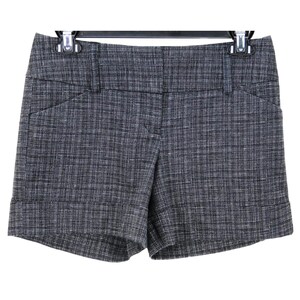 May include: Grey and white tweed shorts with a cuffed hem. The shorts have a tailored design with a button and zip closure, belt loops, and front pockets. The shorts are hanging on a black hanger.