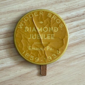 以下が含まれることがあります： 「Widder Bros. Diamond Jubilee  Emaus Pa. 1859-1934」と書かれた黄色の丸いボタンです。