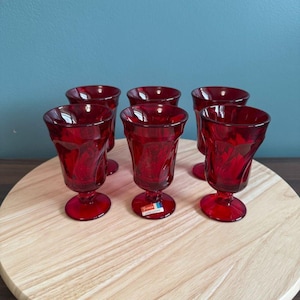 Puede incluir: Seis copas de vidrio rojo con un diseño de vidrio cortado. Las copas están sobre una superficie de madera.