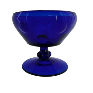 May include: A cobalt blue glass dessert dish with a rounded bowl and a pedestal base. The bowl has a series of circular indentations around the rim. The stem features a decorative bulbous design. The dish is made of transparent glass.